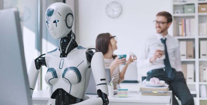 A close-up image of an AI robot working on a computer, while in the background, two supply chain professionals are having a conversation.