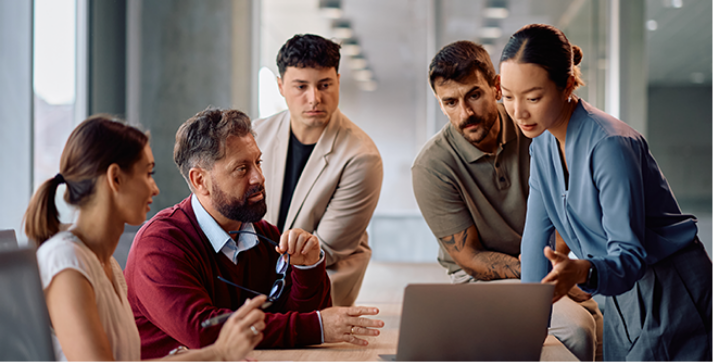 A group of supply chain business professionals reviewing information on a laptop, collaborating on business decisions.