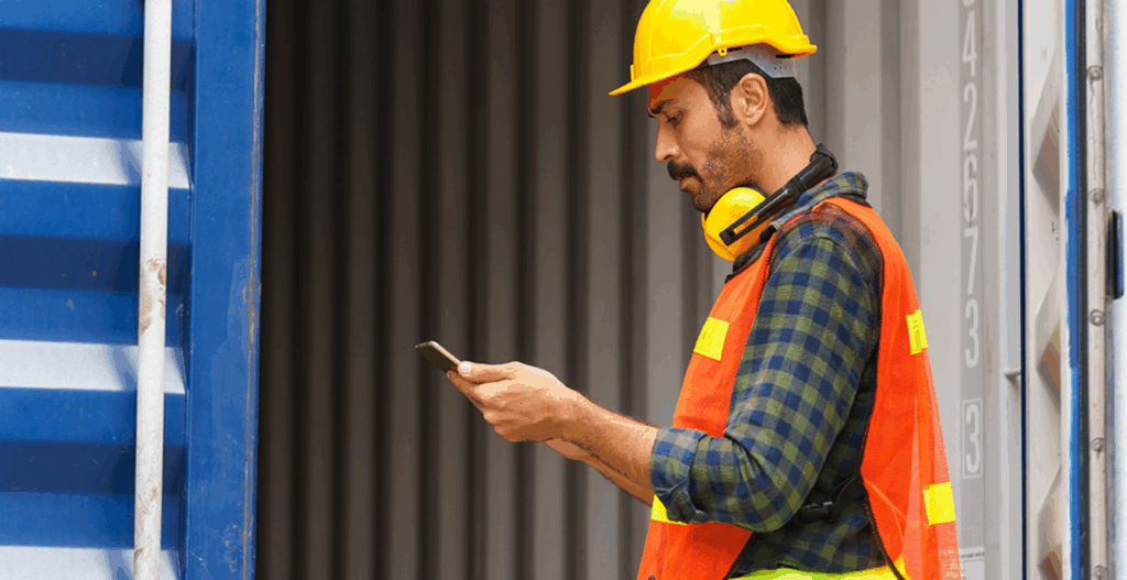 Close-up of a logistics agent holding a tablet, tracking the movement of containers. In the background, the entrance to an open container can be seen.